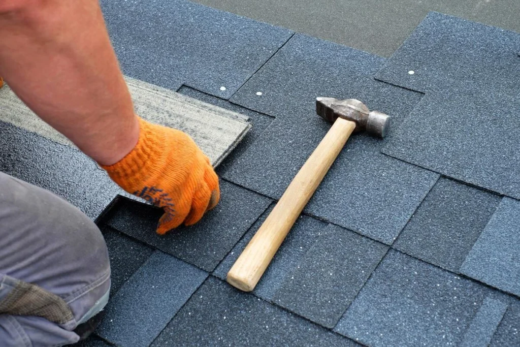 Roofer nailing a new asphalt shingle into place with a hammer