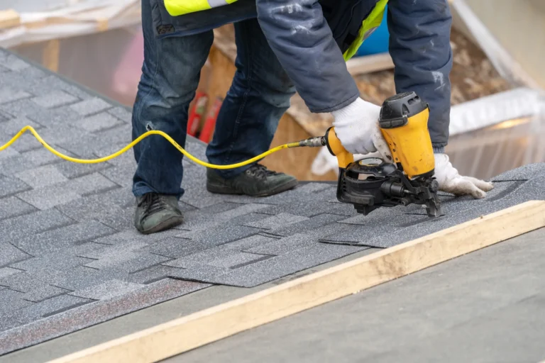 Roofer installing asphalt shingles with a nail gun