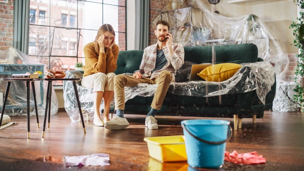 couple in living room with leaking roof and water dripping into bucket
