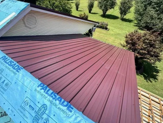 Workers aligning standing seam metal panels on a Lenoir City house roof