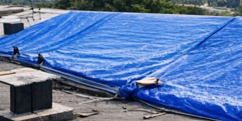 Blue tarp covering a damaged commercial roof as a temporary solution provided by Daniel Hood Roofing for Emergency Commercial Roof Repair services.